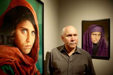 US photographer Steve McCurry poses next to his photos of the "Afghan Girl" named Sharbat Gula at the opening of the "Overwhelmed by Life" exhibition of his work at the Museum for Art and Trade in Hamburg, northern Germany on June 27, 2013. The exhibition comprises some 120 photographs taken between 1980 and 2012 in countries such as Afghanistan, the United States, Pakistan, India, Tibet, Kashmir, Cambodia, Indonesia, Burma and Kuwait. AFP PHOTO / DPA / ULRICH PERREY GERMANY OUT 
RESTRICTED TO EDITORIAL USE, MANDATORY MENTION OF THE ARTIST UPON PUBLICATION, TO ILLUSTRATE THE EVENT AS SPECIFIED IN THE CAPTION (Photo by ULRICH PERREY / DPA / AFP) (Photo by ULRICH PERREY/DPA/AFP via Getty Images)