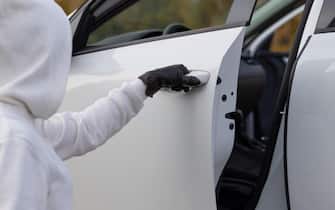 A man in a white sweater and black gloves opens the car door to steal him on a warm autumn day. Selective focus. Close-up
