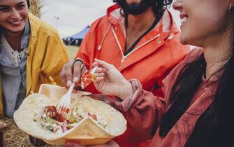 Three friends enjoy sharing some take away  food while at a music festival