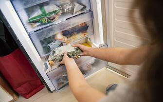Girl taking bag with frozen mixed vegetables from refrigerator.
