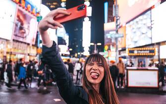Midtown New York, young Taiwanese tourist woman  spending a night in Times Square and sharing on social media with her smart phone.