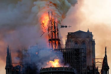 TOPSHOT - The steeple and spire collapses as smoke and flames engulf the Notre-Dame Cathedral in Paris on April 15, 2019. - A huge fire swept through the roof of the famed Notre-Dame Cathedral in central Paris on April 15, 2019, sending flames and huge clouds of grey smoke billowing into the sky. The flames and smoke plumed from the spire and roof of the gothic cathedral, visited by millions of people a year. A spokesman for the cathedral told AFP that the wooden structure supporting the roof was being gutted by the blaze. (Photo by Geoffroy VAN DER HASSELT / AFP)        (Photo credit should read GEOFFROY VAN DER HASSELT/AFP via Getty Images)