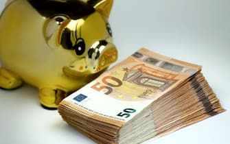 Golden piggy bank with stack of 50 euro banknotes in foreground.