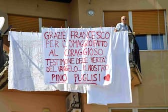 A resident stands on a balcony, by a sheet reading "Thank you Francis for the hommage you paid to the courageous testimony of the Gospel's truth...our Pino Puglisi", in the underprivileged neighbourhood of Brancaccio in Palermo on September 15, 2018 on the occasion of the 25th anniversary of the killing by the mafia of Sicilian priest Pino Puglisi. - Pope Francis pays a one-day pastoral visit on September 15 to the Dioceses of Piazza Armerina and Palermo in Sicily, on the occasion of the 25th anniversary of the killing by the mafia of Sicilian priest Pino Puglisi. (Photo by Andreas SOLARO / AFP)        (Photo credit should read ANDREAS SOLARO/AFP via Getty Images)