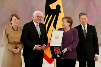 epa10577242 Former German Chancellor Angela Merkel  (2-R) holds the box with the 'Grand Cross of the Order of Merit of the Federal Republic of Germany' as she poses for the media with her husband Joachim Sauer (R), German President Frank-Walter Steinmeier (2-L) and his wife Elke Buedenbender (L) after the awarding ceremony n Berlin, Germany, 17 April 2023.  EPA/FILIP SINGER