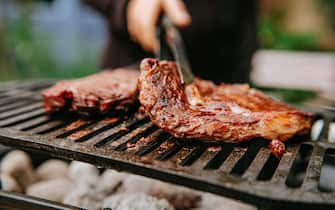 Woman doing BBQ Steaks on a flame grill.