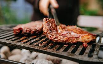 Woman doing BBQ Steaks on a flame grill.