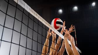 Women volleyball players hands blocking volleyball ball during match at night.