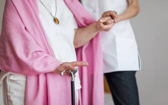 Senior woman with a crutch getting support from nurse. Lower section.