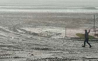 A surfer gestures the shaka sign while running to the Pacific Ocean from the beach as hail and rain fall during a winter storm that blanketed the region in Redondo Beach, California, on February 25, 2023. - Heavy snow fell in southern California as the first blizzard in a generation pounded the hills around Los Angeles, with heavy rains threatening flooding in other places. (Photo by Patrick T. Fallon / AFP) (Photo by PATRICK T. FALLON/AFP via Getty Images)