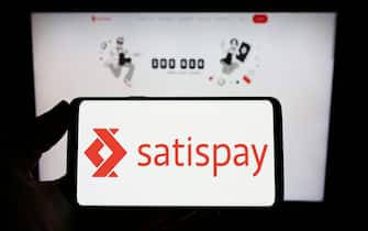 Person holding smartphone with logo of Italian payment company Satispay S.p.A. on screen in front of website. Focus on phone display.