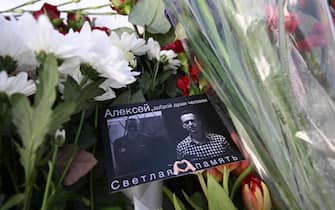 A card with images of late Russian opposition leader Alexei Navalny is seen among flowers left at the Solovetsky Stone, a monument to political repression that has become one of the sites of tributes for Navalny, in Moscow on February 20, 2024, following the death of Navalny in an Arctic prison. (Photo by NATALIA KOLESNIKOVA / AFP)