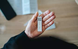 Overhead view of senior Asian woman carrying out a Covid-19 rapid lateral flow test at home. She is holding a positive Coronavirus rapid self test device, feeling worried