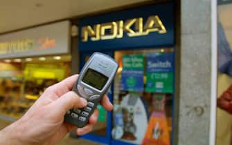A hand holding a Nokia 3210 mobile phone in front of a Nokia shop, in Edinburgh, Scotland. This was a highly popular cellular phone released in 1999.
