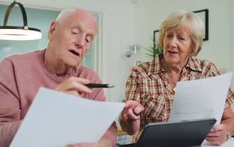 Home, talking and senior couple with paperwork, financial planning and tablet with taxes, pension fund and life policy. Documents, old man or elderly woman with insurance, conversation and investment
