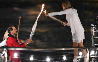 Spain's tennis player Rafael Nadal (L) hands over the Olympics torch to former French tennis player Amelie Mauresmo holding the torch during the opening ceremony of the Paris 2024 Olympic Games in Paris on July 26, 2024. (Photo by Kirill KUDRYAVTSEV / AFP)