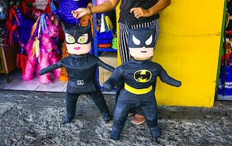 SAN SALVADOR, EL SALVADOR - MARCH 29: A person holds Batman and Catwomen pinatas made by a Salvadoran woman in front of a store on the Avenue Ã¢EspanaÃ¢Â , a street with several blocks full of shops selling and producing Ã¢PinatasÃ¢Â  in the historic center, in San Salvador, El Salvador, on March 29, 2023. Several generations of families support the economy of their homes by working in the production and sale of pinatas on Avenida Espana. The Ã¢pinatasÃ¢Â  are created from wire and paper structures of various figures at the client's choice. Ã¢PinatasÃ¢Â  are filled with sweets and gifts to brighten up family celebrations in many countries around the world. (Photo by Alex Pena/Anadolu Agency via Getty Images)