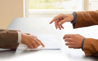 Hands from two businessmen in conversation by a desk. One pointing in papers. Negotiating business or a job interview. - Image