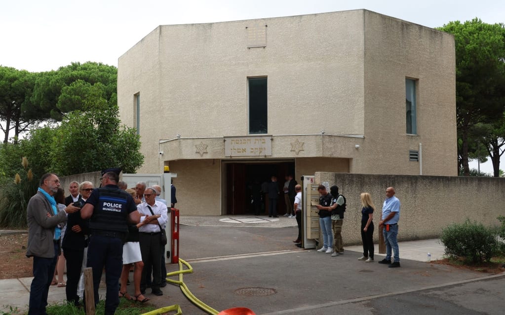 A municipal police officer speaks to bystanders outside of the synagogue which was set on fire and were an explosion of cars occured in La Grande-Motte, south of France, on August 24, 2024. At least two cars, one containing a gas bottle, were set alight on the morning of August 24, 2024, in front of the synagogue in La Grande-Motte, causing an explosion that injured a local policeman, the French gendarmerie and the town's mayor said. (Photo by Pascal GUYOT / AFP) (Photo by PASCAL GUYOT/AFP via Getty Images)