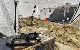 A pair of Teva sandals are seen on a chest in the middle of tents sitting in a muddy desert plain on September 3, 2023, after heavy rains turned the annual Burning Man festival site in Nevada's Black Rock desert into a mud pit. Tens of thousands of festivalgoers were stranded September 3, in deep mud in the Nevada desert after rain turned the annual Burning Man gathering into a quagmire, with police investigating one death.
Video footage showed costume-wearing "burners" struggling across the wet gray-brown site, some using trash bags as makeshift boots, while many vehicles were stuck in the sludge. (Photo by Julie JAMMOT / AFP) (Photo by JULIE JAMMOT/AFP via Getty Images)