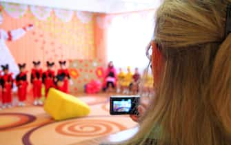 Woman takes pictures of children's morning party. Children in smart suits during performance at matinee in kindergarten