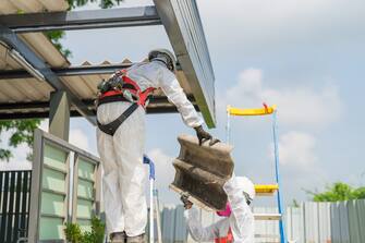 Workers wearing full body protective clothing while working with the asbestos roof tiles. Hazardous waste management and working safety concept. Professional waste disposal.