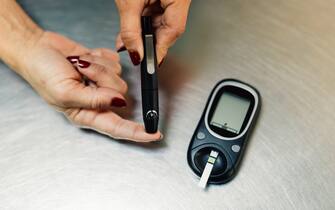 Close up of woman's hands pricking her finger with a lancet in order to test her blood sugar level