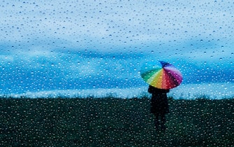 Lonely person holding a rainbow umbrella in the rain