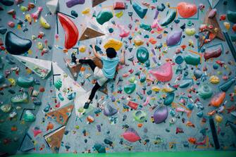 One teenage girl climbing up a bouldering wall at a sport rock climbing gym in Japan
