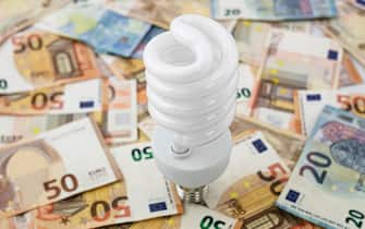 Metaphor about the excessive cost of light, energy and electricity, using a white halogen bulb on a bed of twenty and fifty euro bills