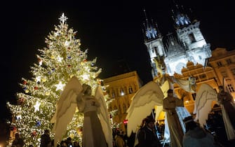 Men wearing angel costumes gesture as people gather around the illuminated Christmas tree at the Old Town Square in Prague on November 29, 2020, amid the ongoing coronavirus Covid-19 pandemic. - The Czech Republic will ease the restrictions aimed at curbing the spread of Covid-19 from December 3, 2020, said on November 29, 2020 the Czech minister of health, Jan Blatny. All restaurants and pubs will be allowed to re-open, with limited indoor seating. Non-essential shops and fitness centers will also re-open as long as there's only one person per 15 square meters. Religious services may resume, and a nighttime curfew will be lifted. (Photo by Michal Cizek / AFP) (Photo by MICHAL CIZEK/AFP via Getty Images)