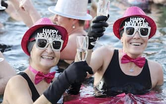 epa10385284 People toast with champagne while swimming in the cold water during the New Year's traditional swimming in the Lake of Geneva at the Bains des Paquis, in Geneva, Switzerland, 01 January 2023.  EPA/SALVATORE DI NOLFI