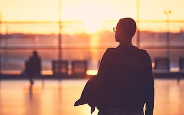 Silhouette of the young man at the airport. Traveler leaves to the gate during golden sunset.