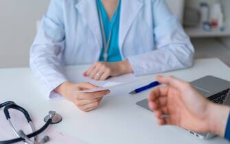 Unrecognizable doctor prescribing pills and drugs to patient. Male hand reaching for piece of paper with pharmacy recommendations. Symptom consultation and getting help