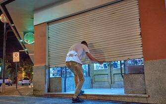 Young man pharmacist standing at open closed drugstore doors and looking outside. for business concept.