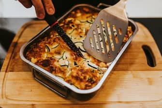 Hands cutting homemade lasagne with zucchini.