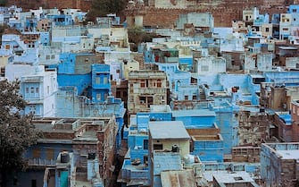 Houses are seen below the walls of Mehrangarh Fort in the old quarters of the Indian city of Jodhpur on March 17, 2016. 
Rajasthan's 'Blue City' Jodhpur is famed for the blue-painted walls of the old city that sits in the shadow of the Mehrangarh Fort. Used to denote Brahmin, or upper-caste, households, discouraging looters if the city ever came under attack, many of Jodhpurs buildings retain the traditional blue paintwork that has come to signify the city.  / AFP / Rebecca CONWAY        (Photo credit should read REBECCA CONWAY/AFP via Getty Images)