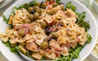 A bowl of bow tie pasta with olives and salad.