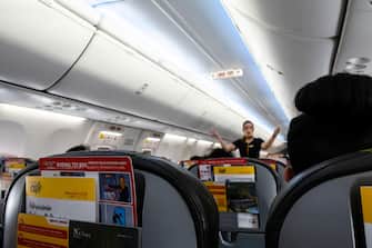 Female flight attendant out of focus  showing emergency exits to passengers sitting in chairs in an  Boeing 737-800