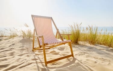 Striped deck chair at sand dunes with marram grass against sea and sunlight