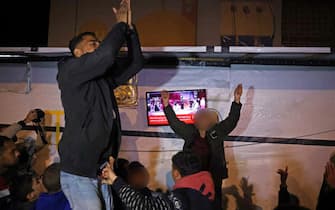 People celebrate while watching a television along a street in Khan Yunis in the southern Gaza Strip on January 15, 2025, amid the ongoing war in the Palestinian territory between Israel and Hamas. Thousands of Gazans celebrated on January 15 as news spread that a ceasefire and hostage release deal had been reached between Israel and Hamas, aimed at ending more than 15 months of war in the Palestinian territory. (Photo by BASHAR TALEB / AFP)