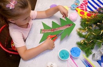 Child makes a greeting card Christmas paper and foam plasticine craft. Made with his own hands. Craft for children. Nice greeting card with a Christmas tree. Top view