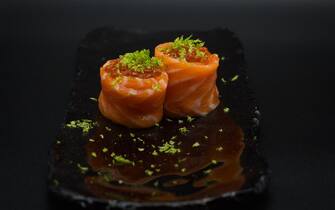 Traditional Japanese Salmon Gunkan, two pieces of wild salmon filet, fresh grated lime and salmon caviar served in black plate with black background.