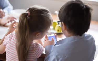 Rear view children using smartphone sitting in the kitchen