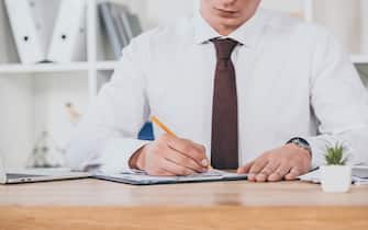 cropped view of businessman filling in compensation claim at workspace
