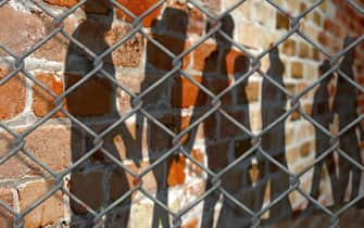 Shadows of people on a wall behind a fence