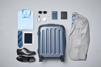 Directly above shot of businesswear with travel accessories. Formalwear and luggage is arranged on gray background. Flat lay of traveler's personal belongings.