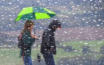 Abstract of a couple walking in rain with an umbrella, seen through a window covered in rain droplets. Wet weather UK.