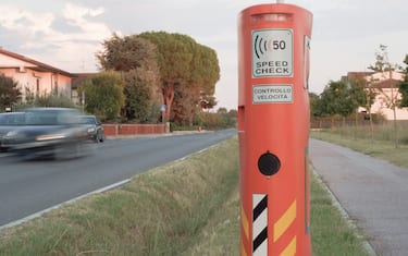 Italy: a car drives along a street of a village in the countryside, passing by a speed camera. Some motion blur. "Controllo velocità" is "speed check" in Italian