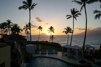 Sunset at Wailea Beach, as viewed from the Four Seasons Resort Maui at Wailea, palm trees and pool visible, Wailea, Maui, Hawaii, 2016. (Photo by Smith Collection/Gado/Getty Images).